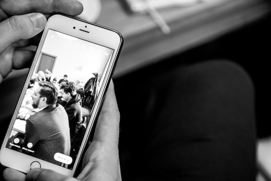 Podgląd telefonu komórkowego, na którym widać zdjęcie osób siedzących wokół prostokątnego stołu; zdjęcie czarno-białe