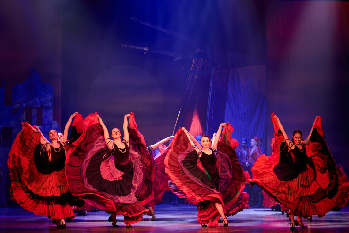 Tancerki w czerwonych sukienkach w trakcie tańca, rozłożyste, falbaniaste spódnice unoszą do góry