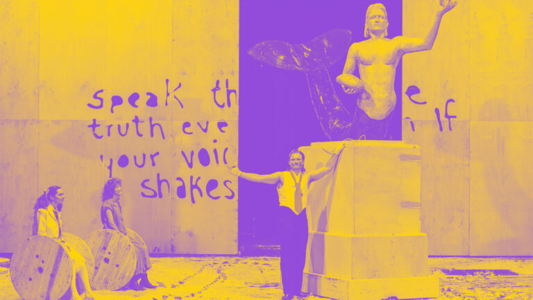 Na środku wielki pomnik syreny w wersji męskiej, przy nim stoi mężczyzna o takiej samej twarzy, z boku siedzą dwie kobiety i przyglądają się - zdjęcie w barwach fioletu i żółci