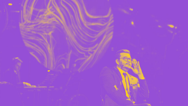 Mężczyzna siedzący na krześle, na drugim planie mężczyzna grający na organach - zdjęcie w barwach fioletu i żółci