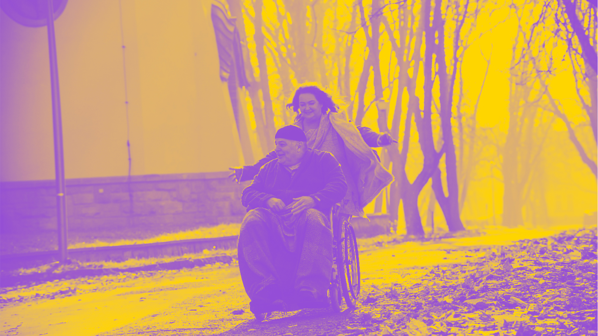 Mężczyzna siedzący na wózku inwalidzkim, za nim kobieta, która go prowadzi, jednak ręce ma rozłożone, nie trzyma wózka - zdjęcie w barwach fioletu i żółci