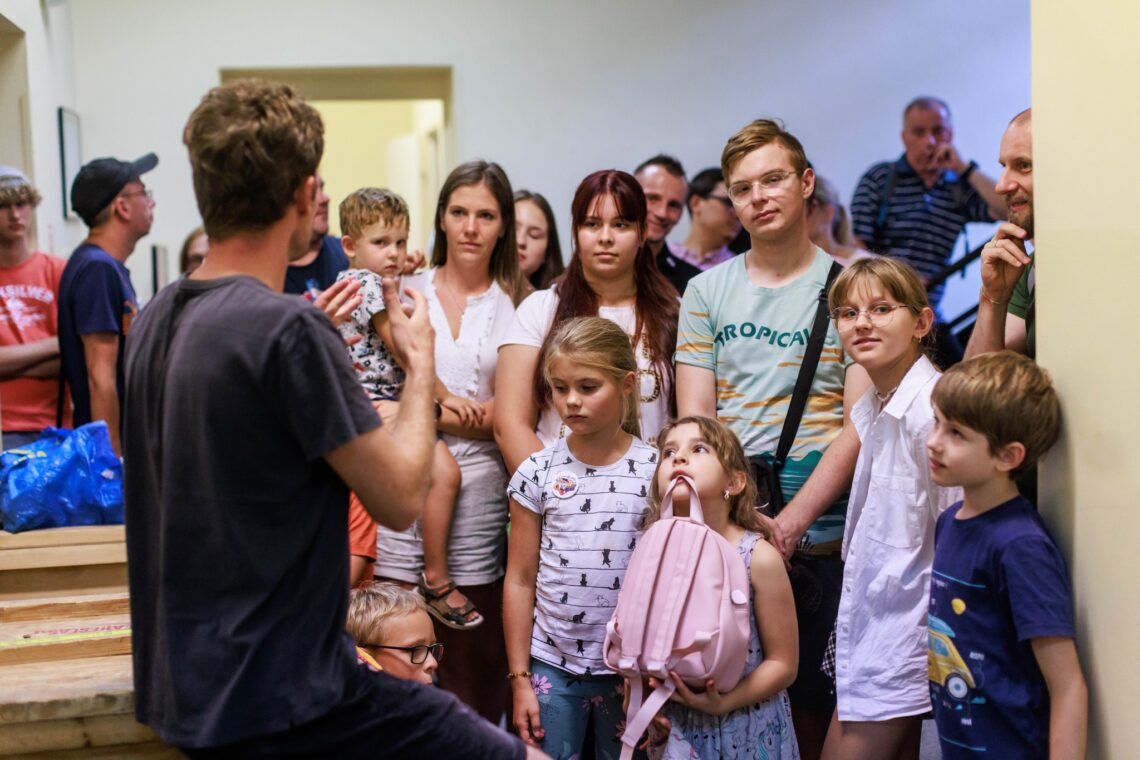 Grupa osób w różnym wieku w trakcie zwiedzania Teatru, osoby stoją razem, jeden obok drugiego w korytarzu