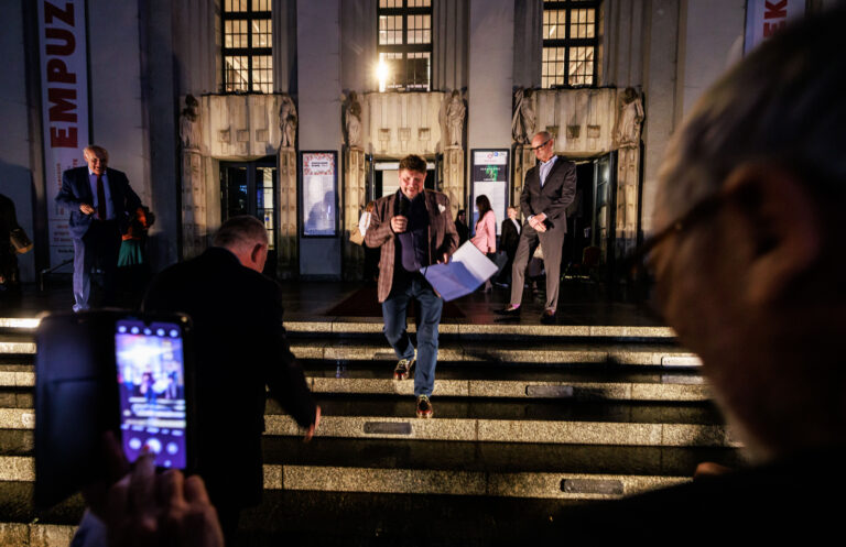 Po schodach przed budynkiem Teatru Śląskiego schodzi Dyrektor Teatru Śląskiego Robert Talarczyk, widoczne są metalowe tabliczki przytwierdzone do podstopni