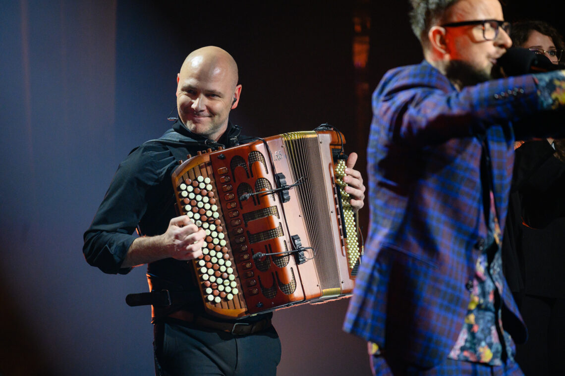 Marcin Wyrostek grający na akordeonie, przed nim do mikrofonu śpiewa Piotr Kupicha