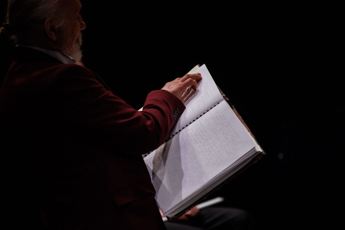A man in a burgundy jacket touches a book with his fingers, in which dots are embossed on the white pages - the Braille alphabet