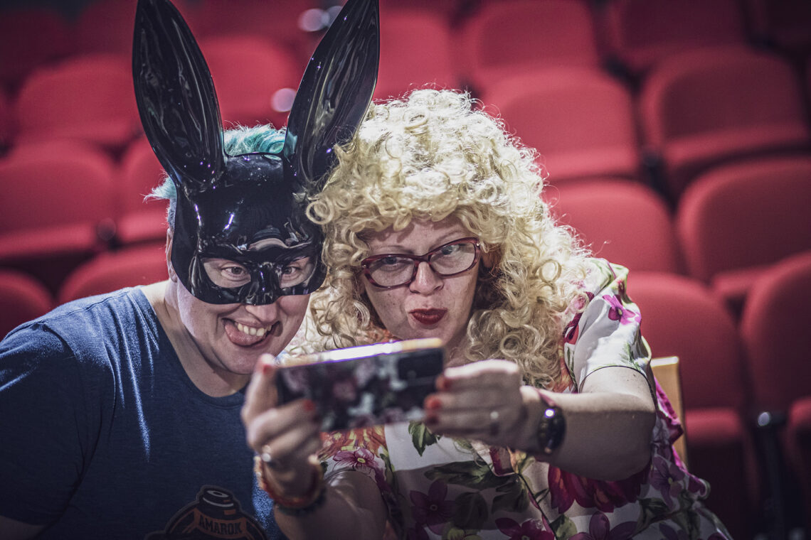 Kobieta w czarnej masce królicza oraz kobieta w blond kręconych włosach robiące sobie wspólne zdjęcie selfie