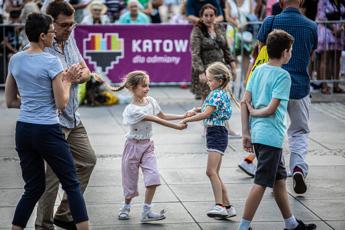 W centrum dwie dziewczynki w trakcie tańca w parze trzymając się za ręce, obok tańcząca para