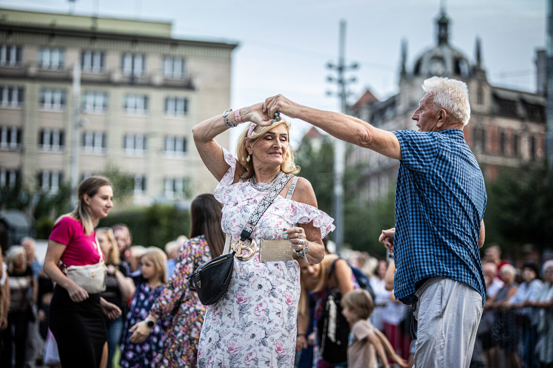 Starsza kobieta i mężczyzna tańczący w parze, kobieta w trakcie obrotu, trzymają się za dłoń uniesioną w górze