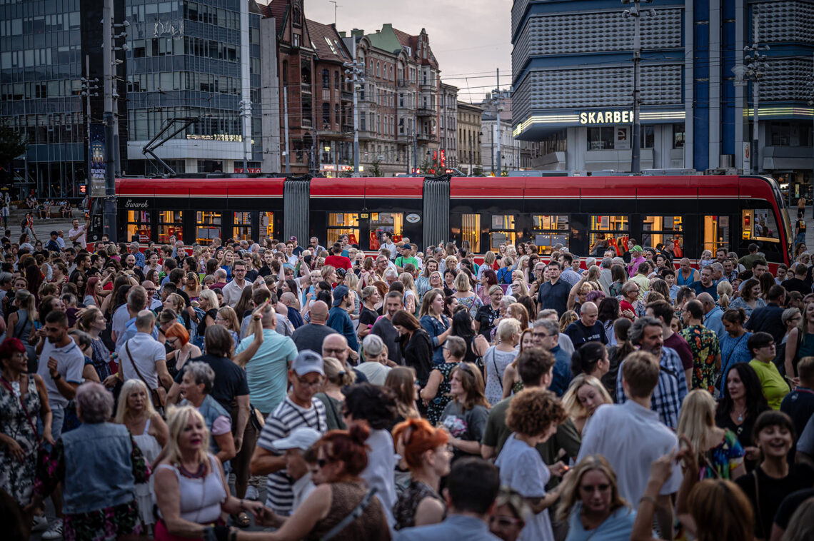 Tłum osób, w tle przejeżdżający tramwaj oraz budynki w centrum miasta