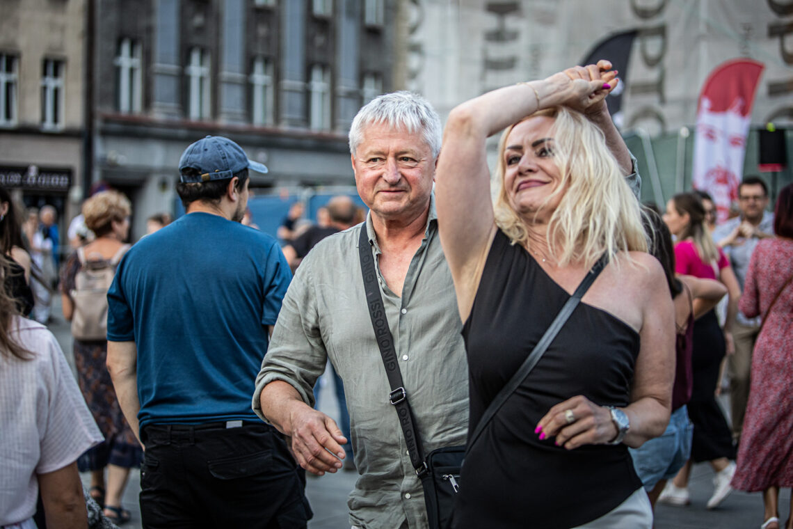 Kobieta i mężczyzna w trakcie tańca, kobieta w trakcie obrotu, oboje są zwróceni twarzą do obiektywu