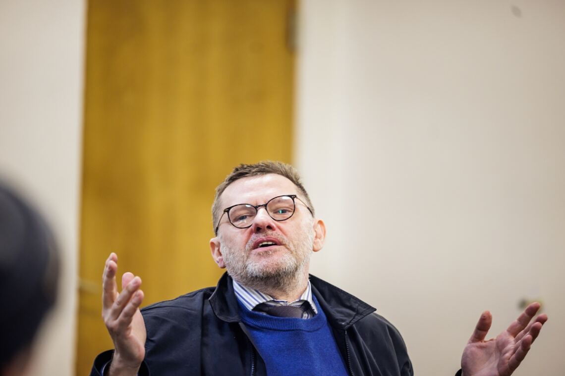Profesor siedzący z uniesionymi dłońmi na wysokości klatki piersiowej
