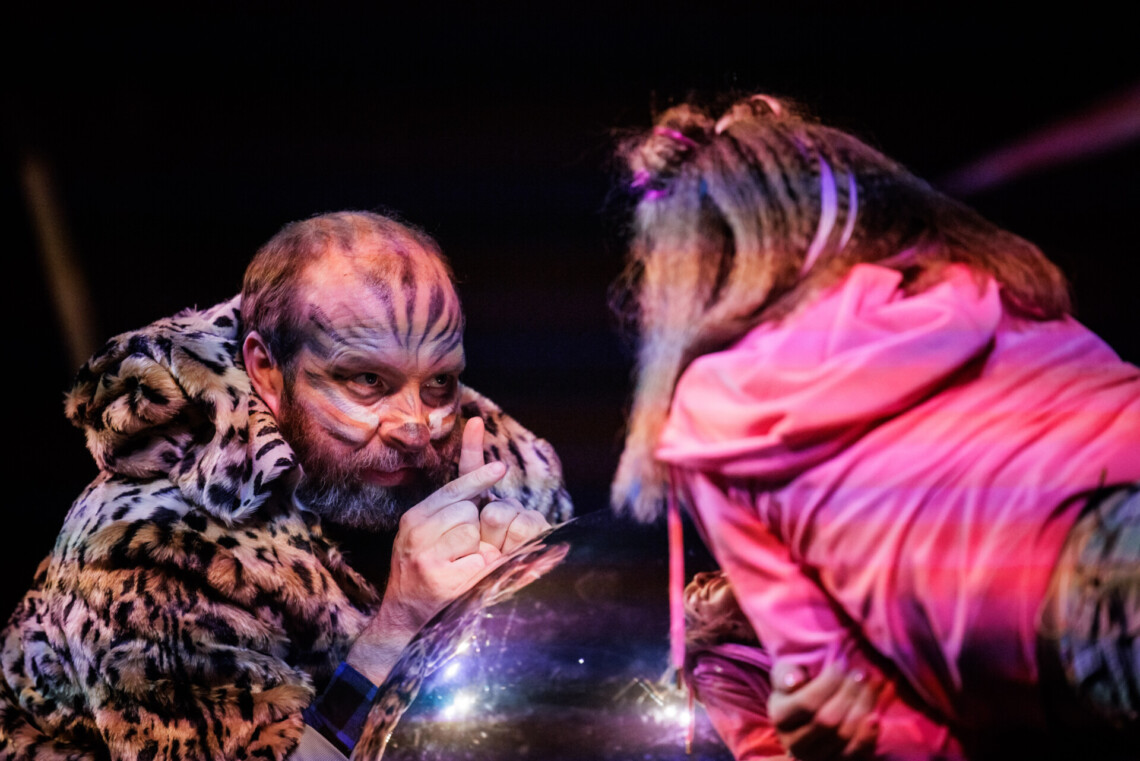 Dwie postaci naprzeciwko siebie, mężczyzna widziany od przodu ma ucharakteryzowaną twarz i kostium drapieżnego kota, naprzeciw niego dziewczyna widziana od tyłu