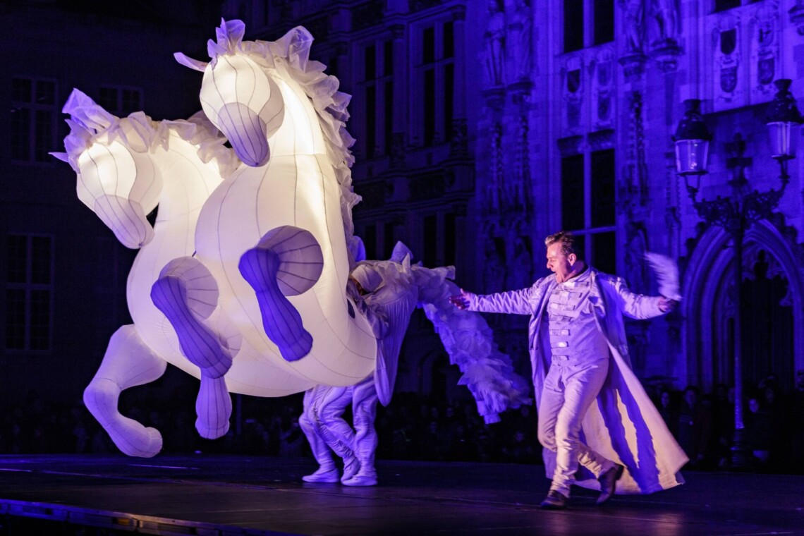 Two large, inflatable, illuminated horses, a man standing next to them, blue background