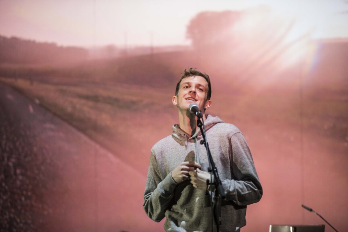 A man in a hoodie standing next to a microphone on a stand