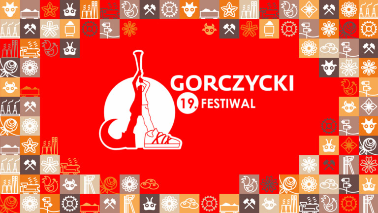 Biała grafika na czerwonym tle: narysowana postać w dwóch różnych butach, dmuchająca do trąbki skierowanej ku górze, z boku napis Gorzycki 19. Festiwal; wokół grafiki ramka z małych kwadracików w różnych kolorach (odcienie pomarańczowego i brązowego) przedstawiające obrazki związane ze Śląskiem, np. szyb górniczy, wagon z węglem, kluski śląskie
