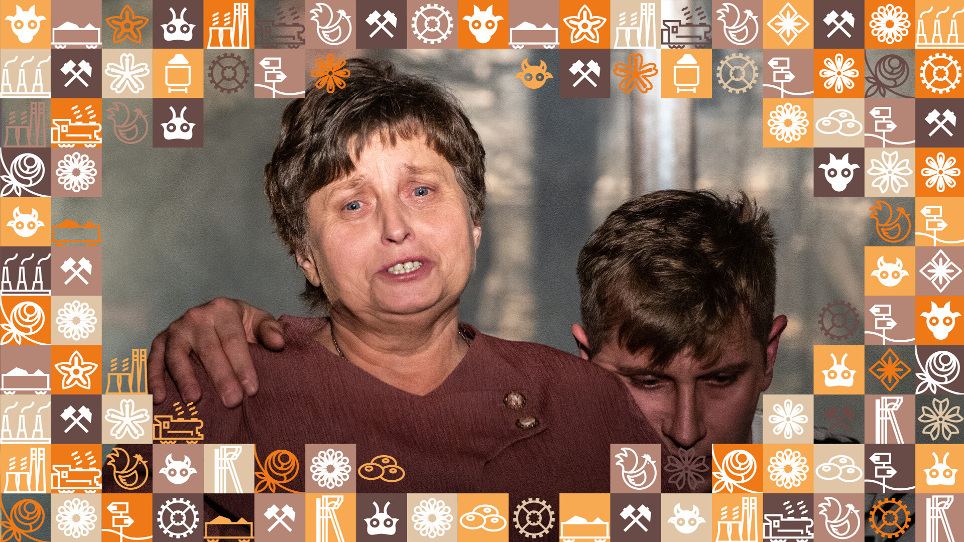 Kobieta z zatroskanym wyrazem twarzy, za nią mężczyzna z pochyloną głową, opiera dłoń na jej ramieniu; wokół zdjęcia ramka z małych kwadracików w różnych kolorach (odcienie pomarańczowego i brązowego) przedstawiające obrazki związane ze Śląskiem, np. szyb górniczy, wagon z węglem, kluski śląskie