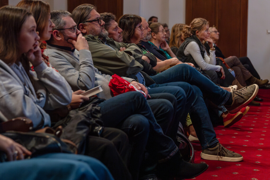 Osoby siedzące w pierwszym rzędzie Dużej Sceny, ujęcie od dołu na równi z siedzącymi osobami