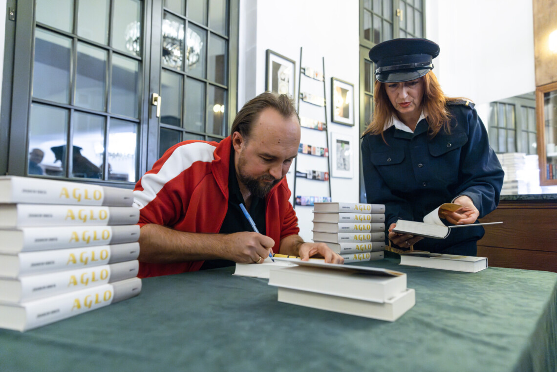Zbigniew Rokita podpisujący swoją książkę, obok niego stoi Barbara Lubos w stroju tramwajarki i otwiera mu książkę na stronie do podpisu