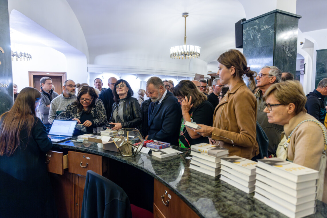 Osoby stojące wokół lady Sklepiku Pan Stanisław, za nimi tłum osób
