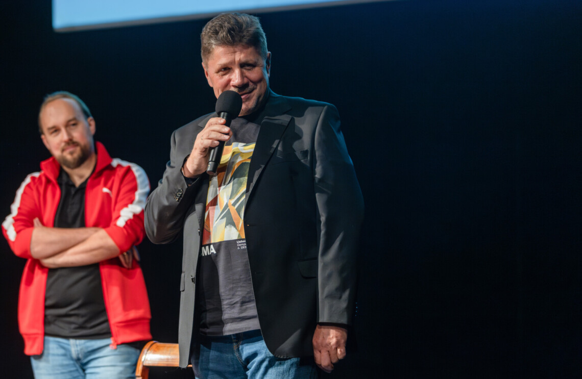 Dyrektor Robert Talarczyk przemawiający na stojąco do mikrofonu, patrzy w bok, na drugim planie stoi Zbigniew Rokita