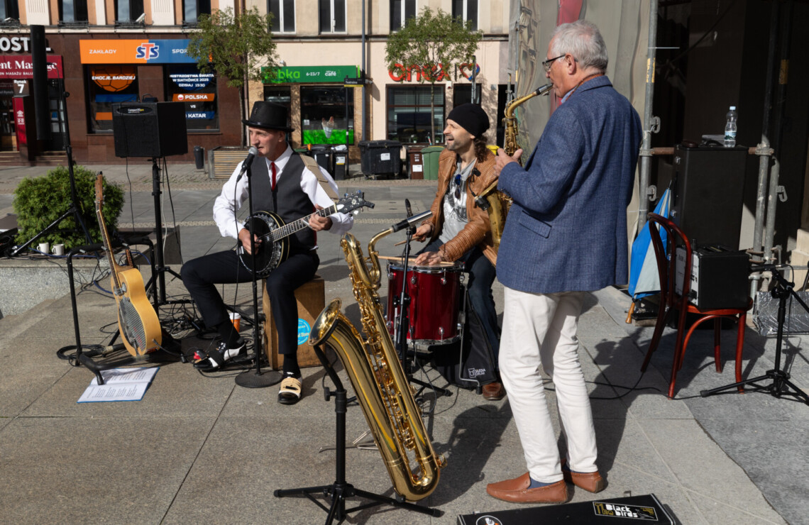 Trzech mężczyzn w trakcie koncertu na zewnątrz, ujęcie z boku