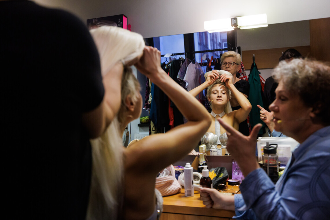 Pomieszczenie damskiej garderoby. Dwie aktorki siedzą przed lustrem. Garderobiana pomaga zakładać perukę Ninie Batovskiej, obok niej siedzi Violetta Smolińska i spogląda na nią.