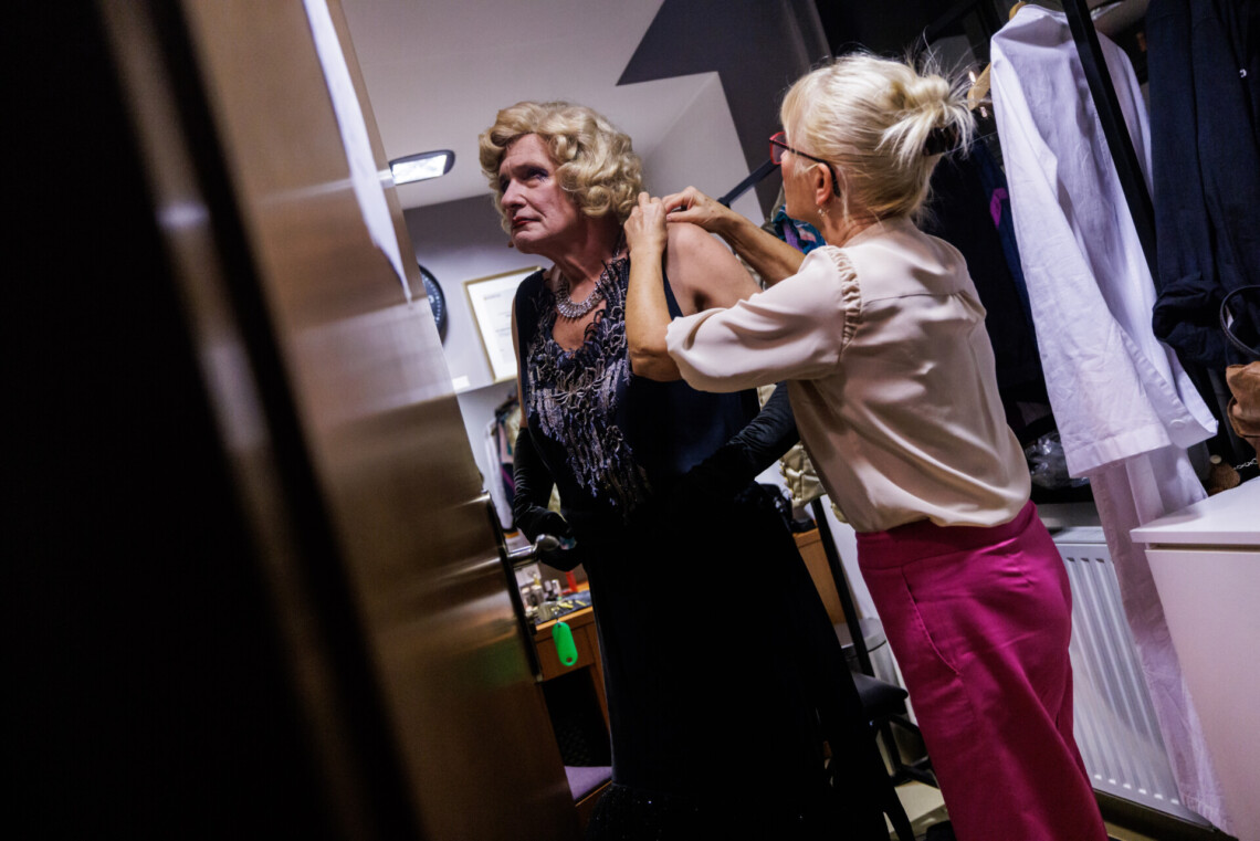 Garderobiana za kulisami pomaga ubrać się w strój kobiecy Andrzejowi Dopierale.