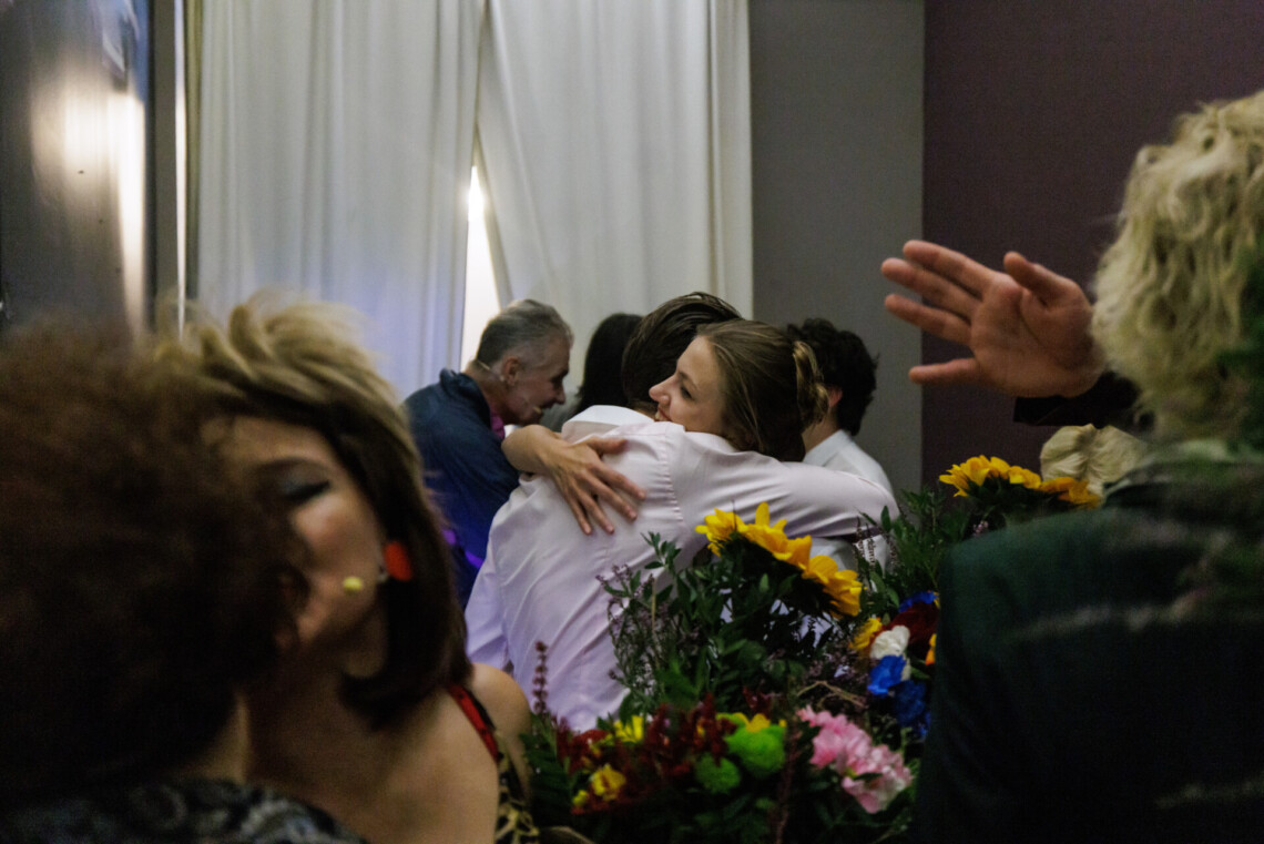 Aktorzy za kulisami po spektaklu, w centrum dwójka aktorów obejmuje się