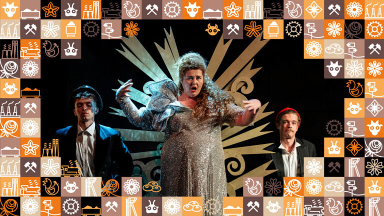 W centrum kobieta w srebrnej, święcącej, ozdobnej sukni, po jej bokach niżej stoi dwóch mężczyzn; wokół zdjęcia ramka z małych kwadracików w różnych kolorach (odcienie pomarańczowego i brązowego) przedstawiające obrazki związane ze Śląskiem, np. szyb górniczy, wagon z węglem, kluski śląskie