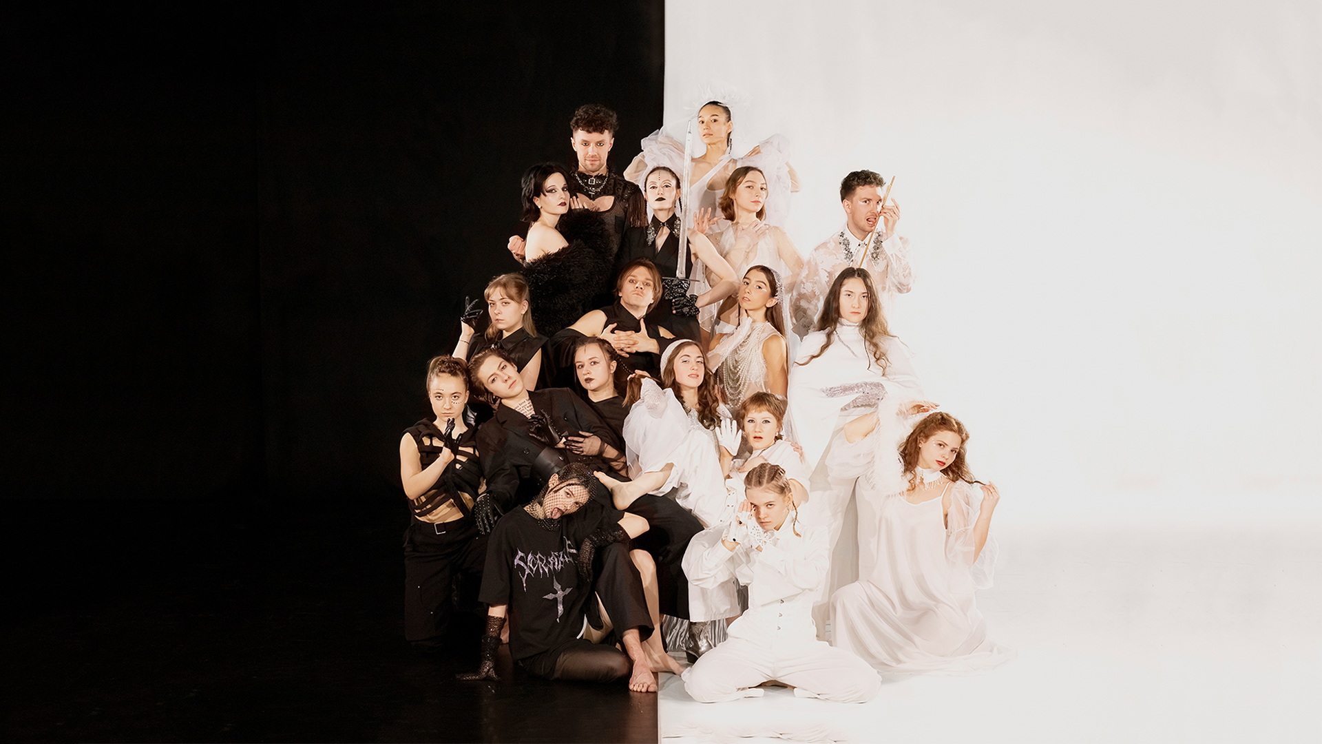 Grupowe zdjęcie osób ustawionych w formie piramidy, z lewej stronie na czarnym tle osoby ubrane na czarno, z prawej strony na białym tle osoby ubrane na biało