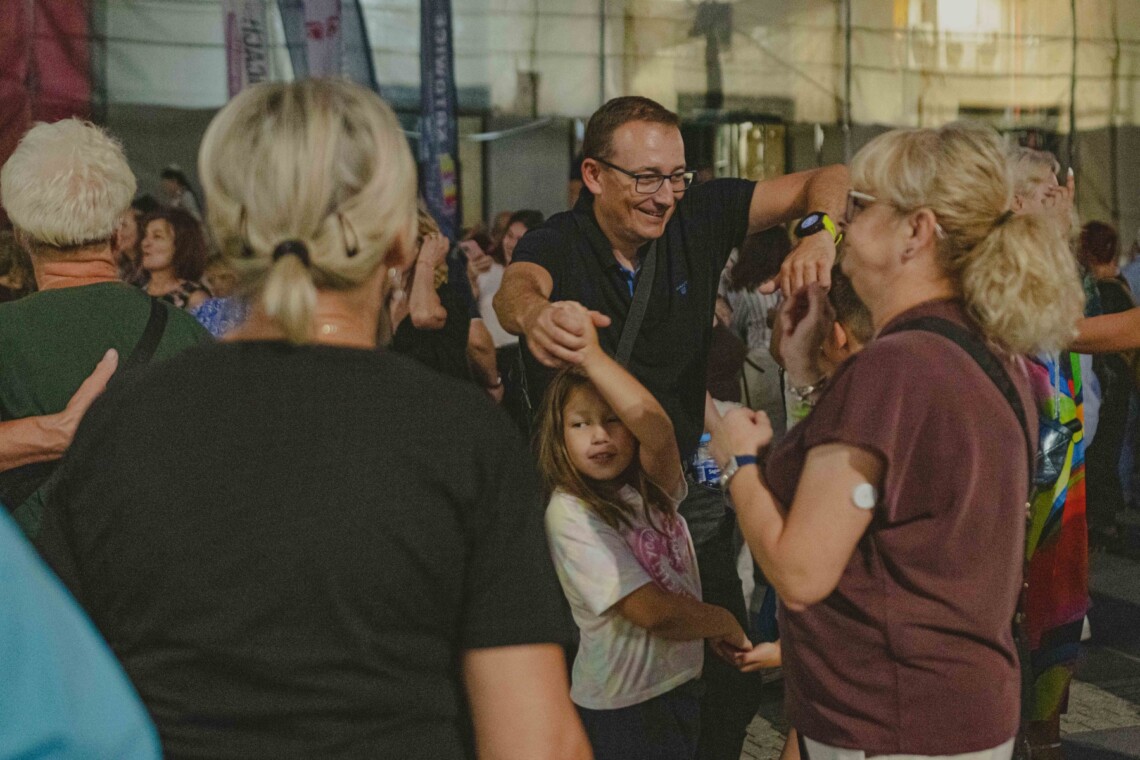 Mężczyzna w trakcie tańca z kobietą i dziewczynką, są w trakcie obrotu