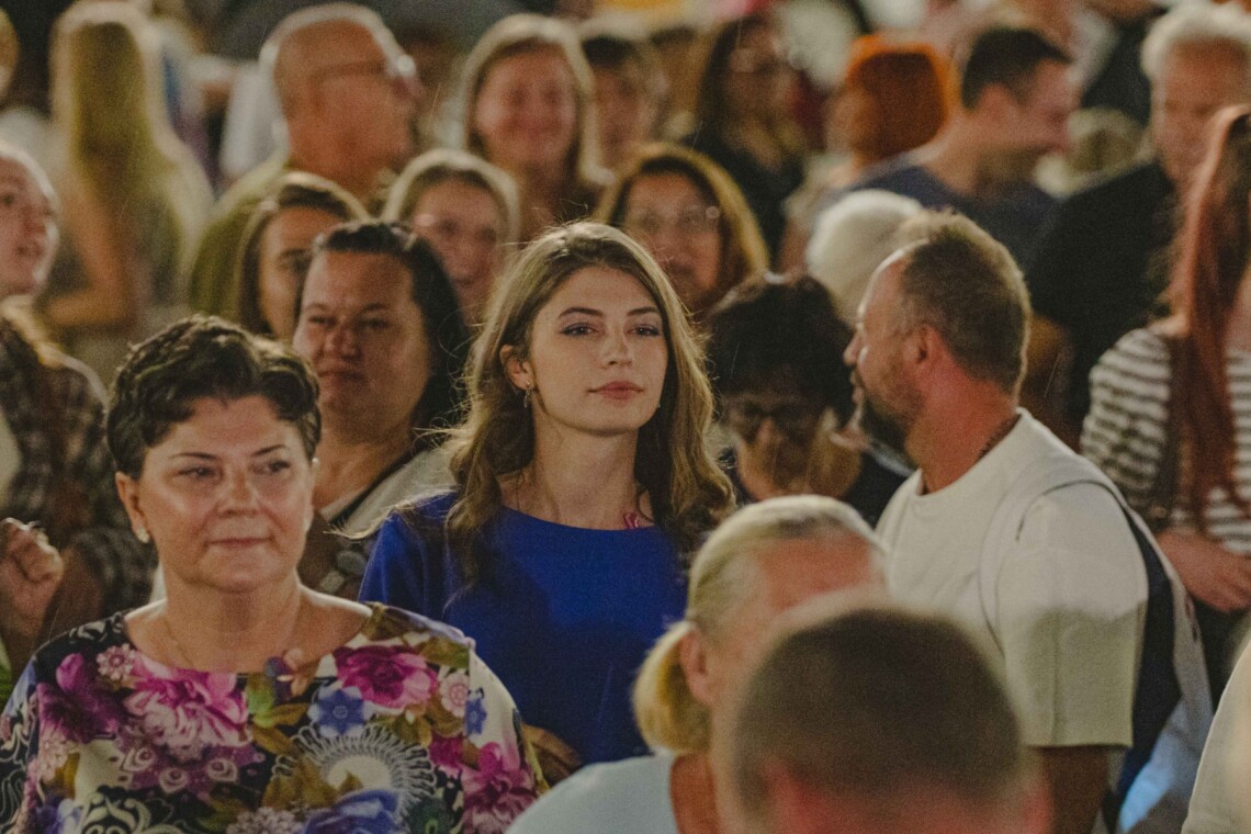 Grupa stojących osób, w centrum wyróżnia się kobieta w niebieskiej bluzce