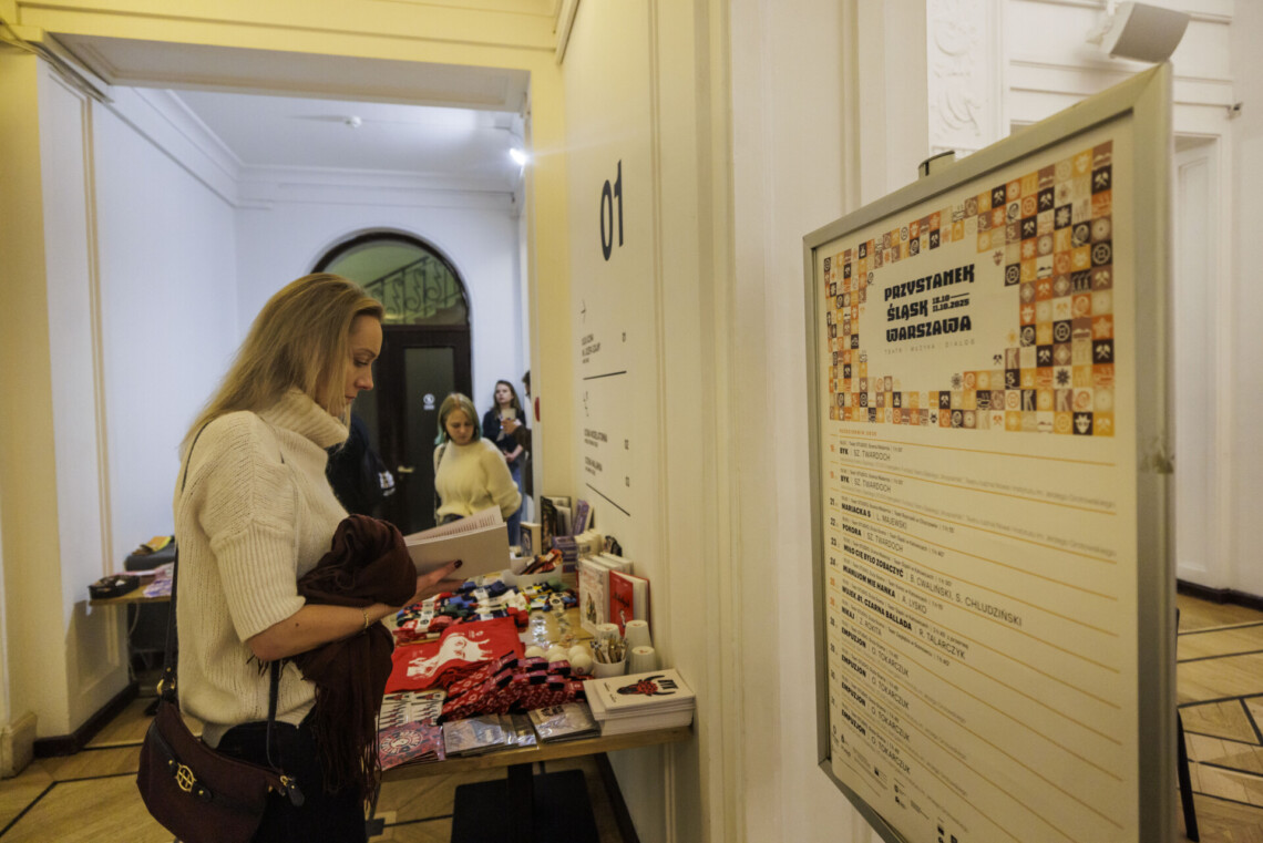 Kobieta przeglądająca program spektaklu Byk we foyer, przed nią plakat Przystanek Śląsk Warszawa