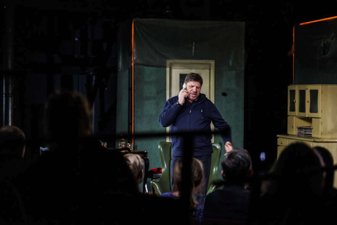 Mężczyzna w dresie rozmawiający przez lelefon, na pierwszym planie osoby siedzące na widowni