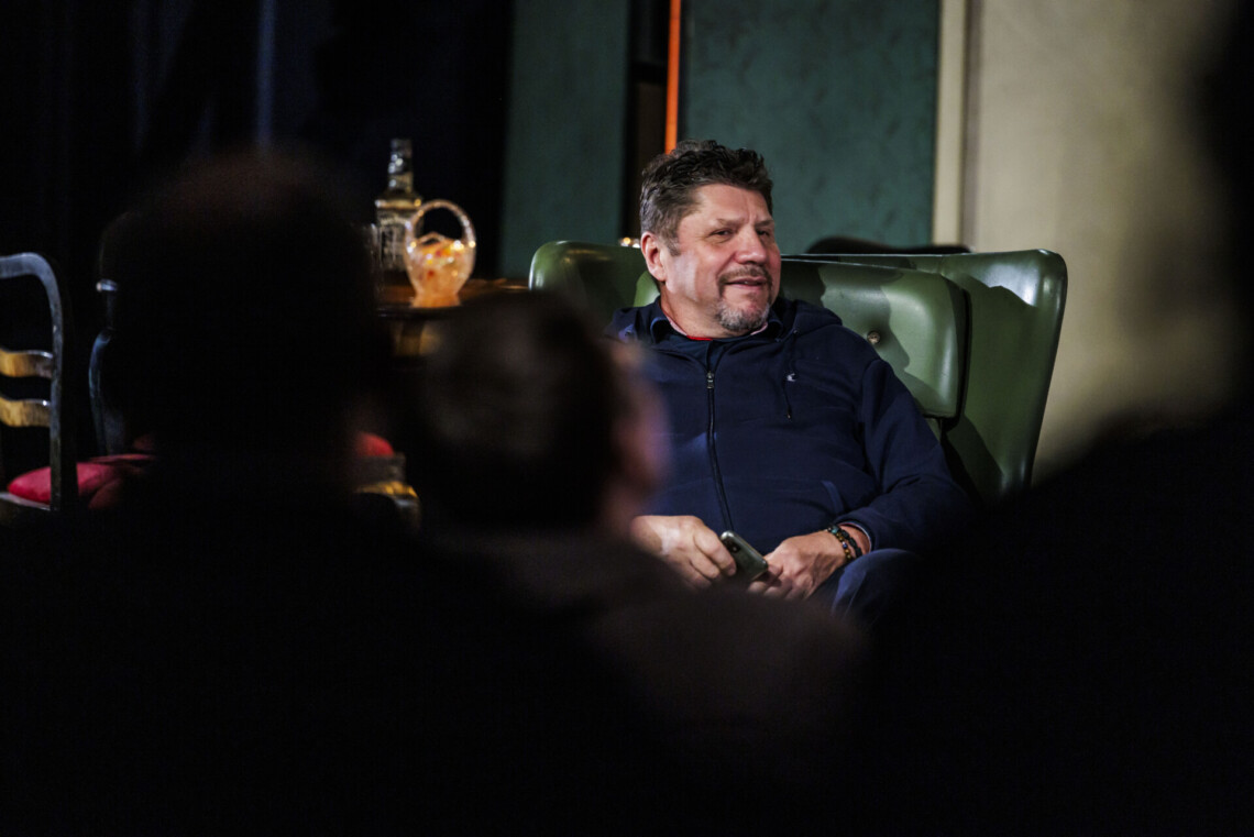 Mężczyzna siedzący w zielonym fotelu, w dłoniach trzyma telefon