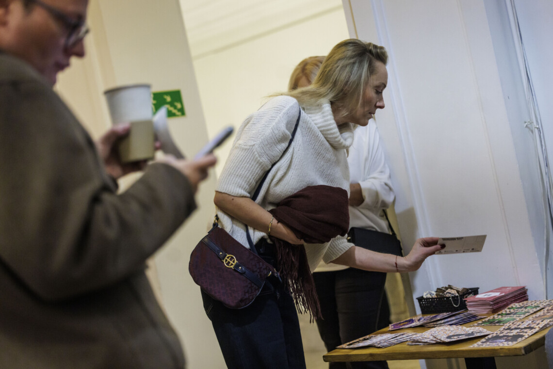 Dwie kobiety przy stoliku z promocyjnymi ulotkami, jedna z nich pochyla się nad stolikiem przysłaniając drugą