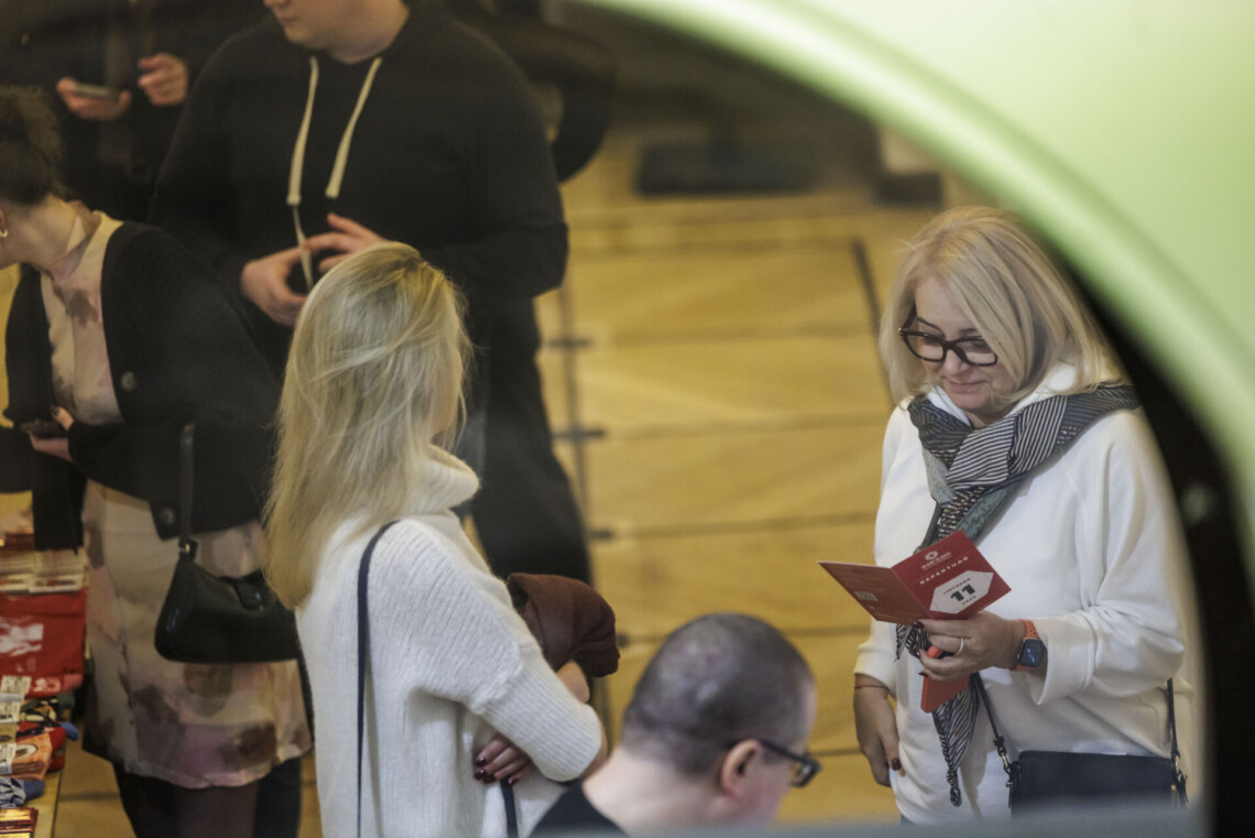 Osoby stojące w foyer, w centrum dwie kobiety stojące naprzeciwko siebie, jedna z nich przegląda ulotkę repertuarową Teatru Śląskiego