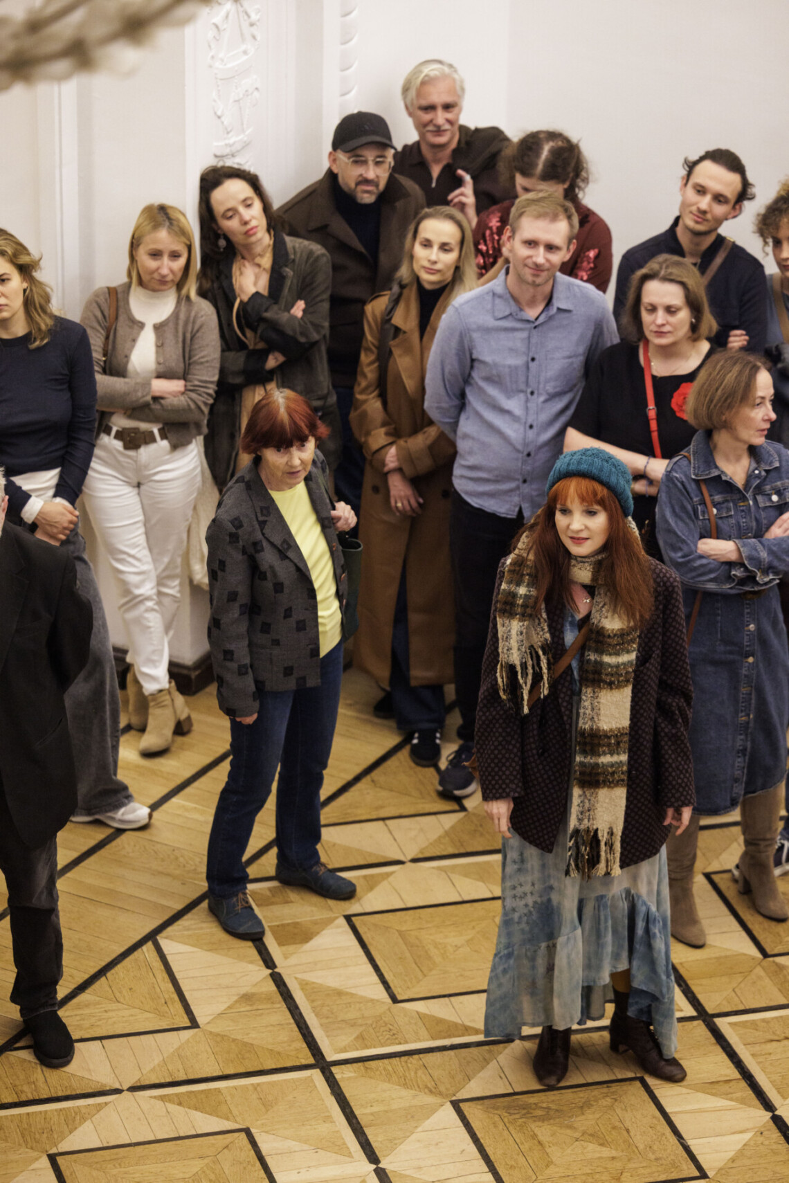 Grupa osób w pomieszczeniu, na przodzie aktorka Agnieszka Radzikowska w kurce, szaliku i czapce, scena ze spektaklu