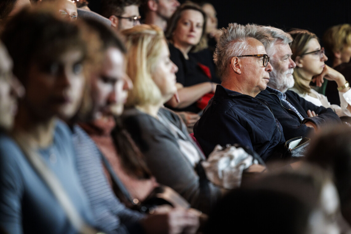 Osoby siedzące na widowni, ostrość na drugiej połowie zdjęcia - dwóch mężczyzn