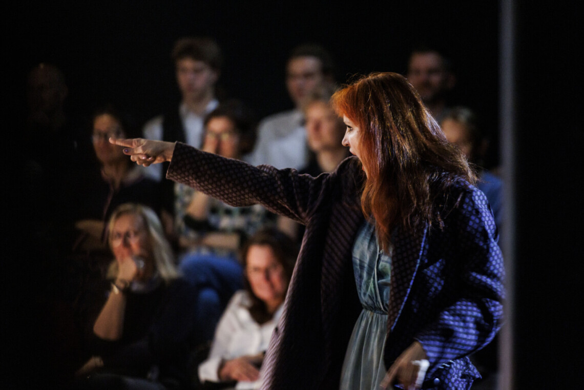 Kobieta w wyciągnięta do przodu prawa ręką i palcem skazującym, ma szeroko otwarte usta