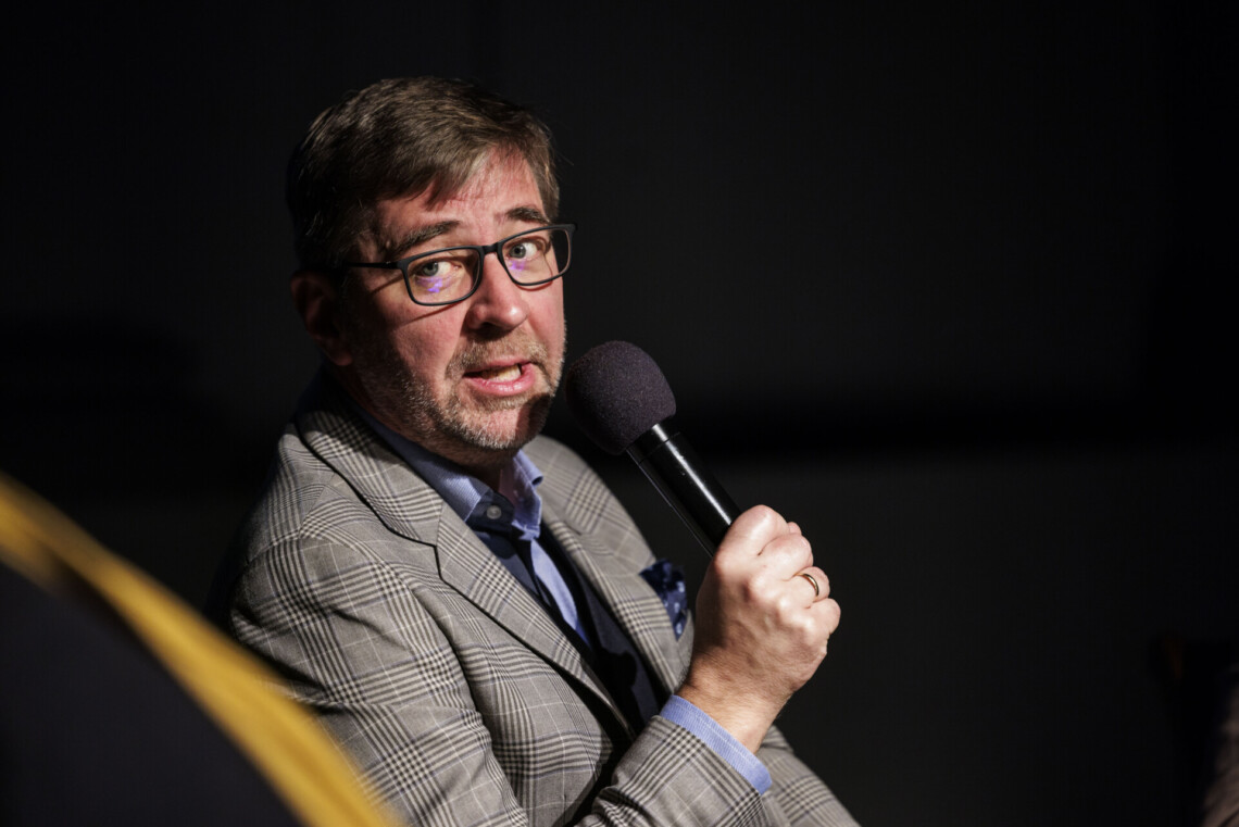 Do mikrofonu przemawia Krystian Węgrzynek, ujęcie z boku, tło czarne