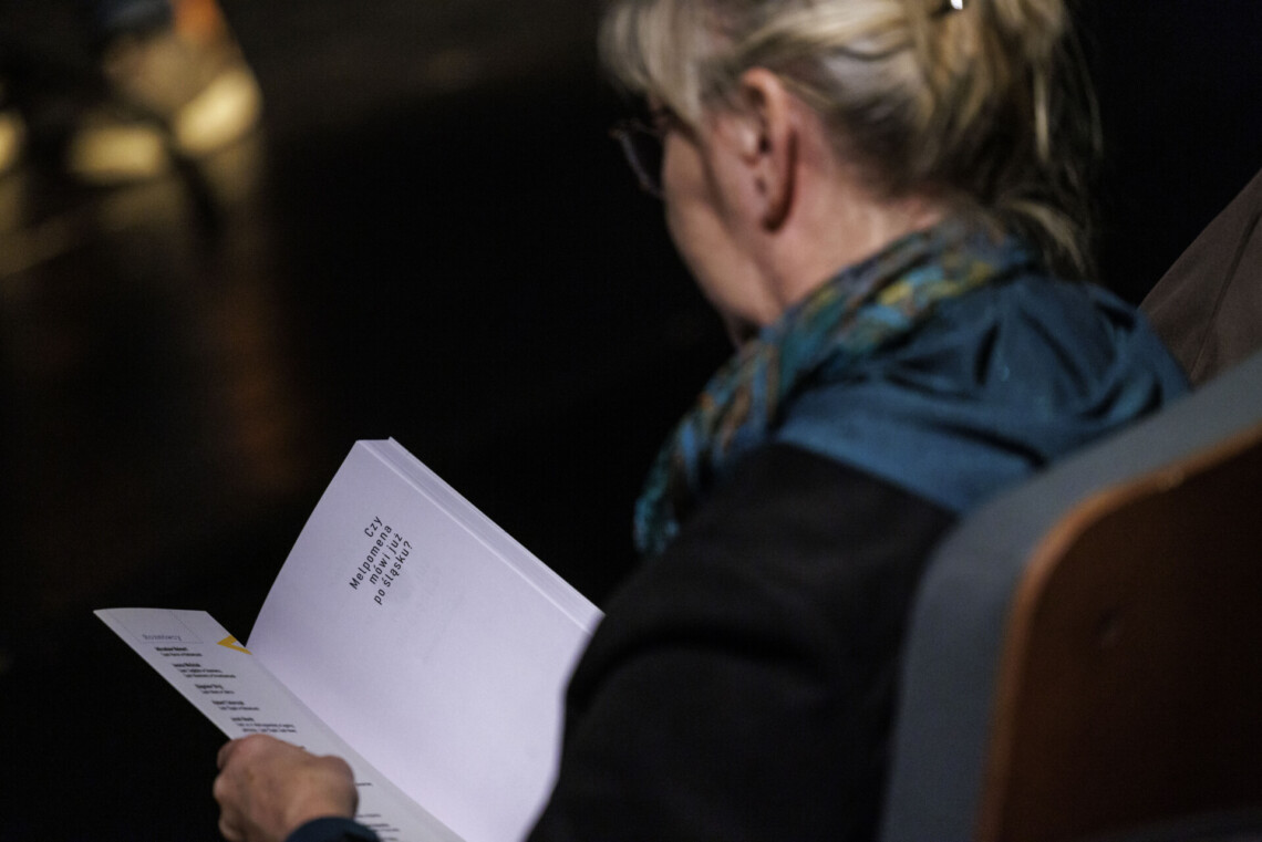 Kobieta na widowni przeglądająca książkę "Czy Melpomena godo po śląsku", ujęcie zza pleców