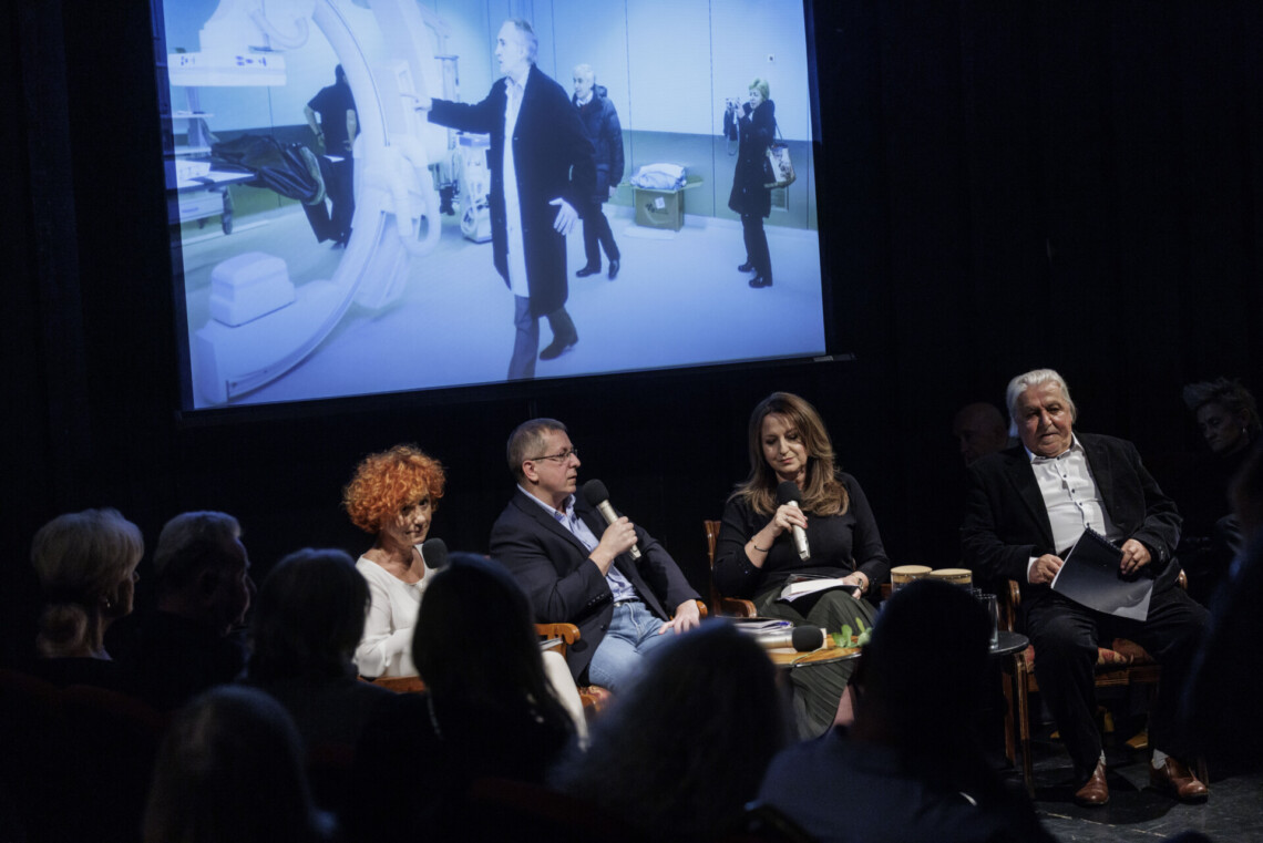 Na scenie cztery osoby siedzące na krzesłach, za nimi na ekranie zdjęcie profesora Zembali przechadzającego się po pomieszczeniu z dużą , krągłą aparaturą medyczną