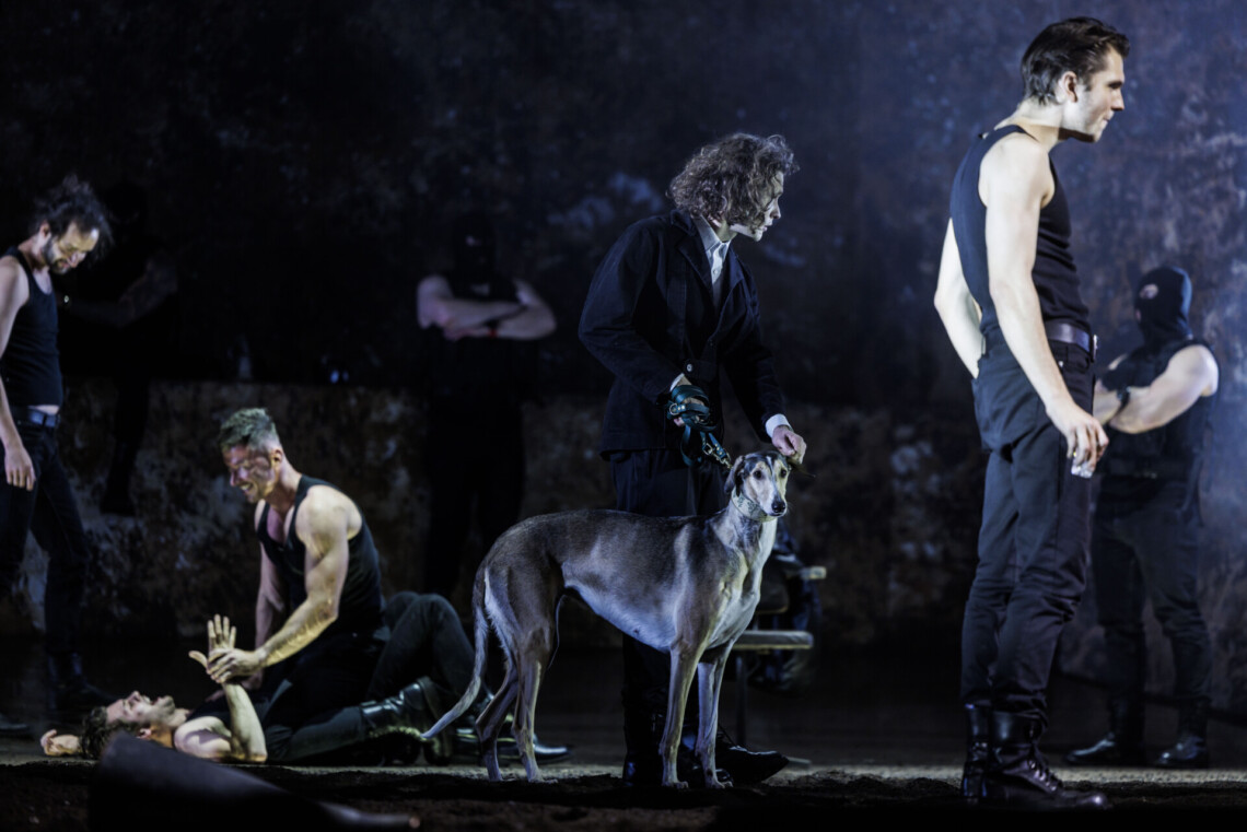 Mężczyźni ubrani na czarno, w centrum mężczyzna z psem na smyczy