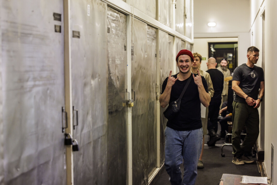 Osoby za kulisami, korytarzem idzie mężczyzna wykonujący dłońmi gest