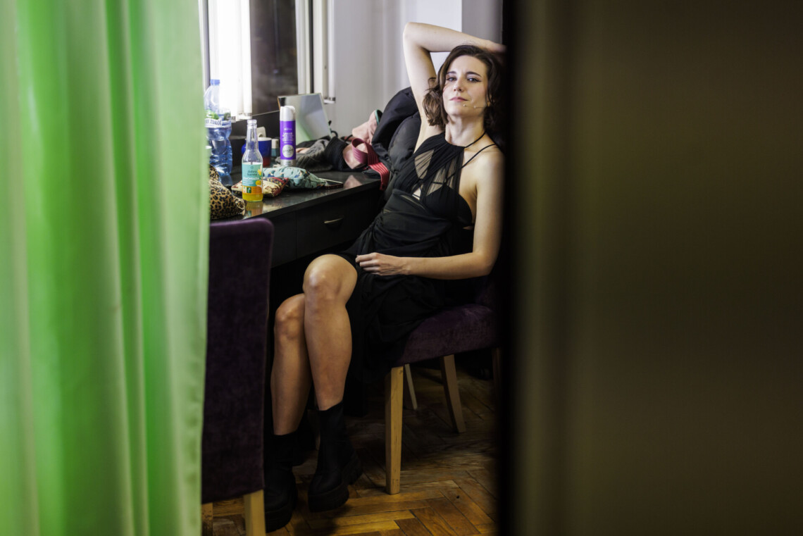 Aktora w czarnej sukience siedząca przy toaletce w garderobie, patrzy w obiektyw
