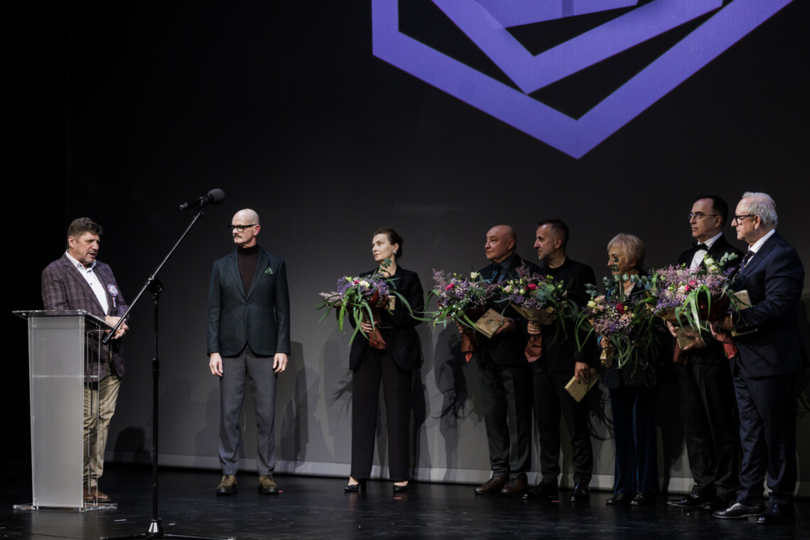 Od lewej Dyrektor Robert Talarczyk oparty o mównicę oraz Dyrektor Bogusław Jasiok. Po prawej stoją przedstawiciele Rady Mecenasów z upominkami w dłoniach oraz kwiatami.