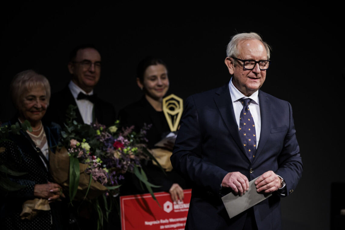 Przedstawiciel Rady Mecenasów stoi w szarą kopertą w dłoni za nim stoją członkowie Rady oraz Aleksandra Bernatek z nagrodą.