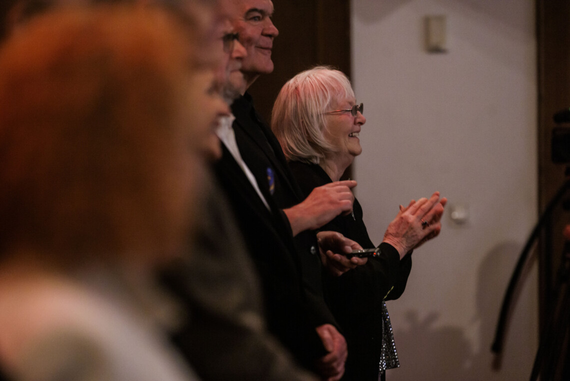 Osoby stojące w pierwszym rzędzie na widowni. W śród nich wyróżnia się aktorka Bogusława Murzyńska. Ujęcie z boku.