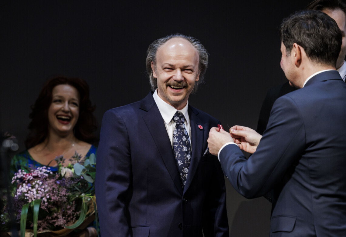 Wojewoda Marek Wójcik przypina odznaczenie Markowi Rachoń. Za nimi stoi uśmiechnięta Barbara Lubos.